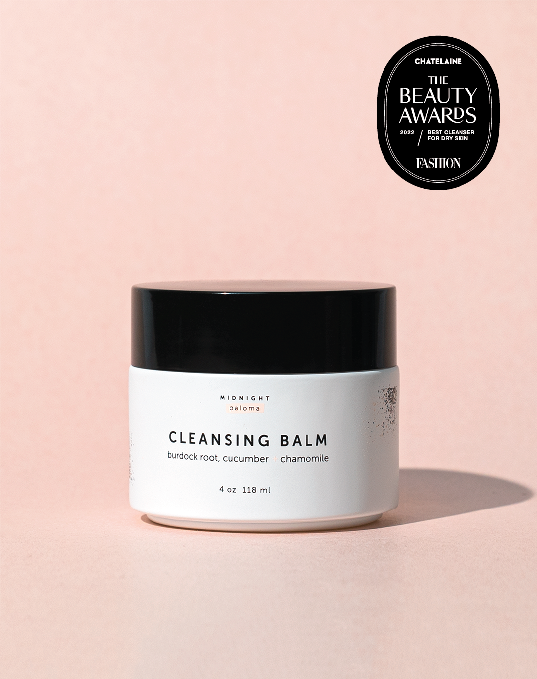 A jar of cleansing balm with a label that reads 'Cleansing Balm' and lists burdock root, cucumber, and chamomile as ingredients. There is a seal of approval from a beauty awards ceremony displayed in the top right corner.